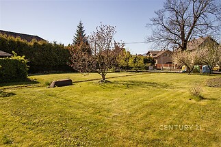 Prostorná zahrada s udržovaným trávníkem, vzrostlými stromy a klidnou atmosférou, ideální pro rodinné aktivity a relaxaci v přírodním prostředí.