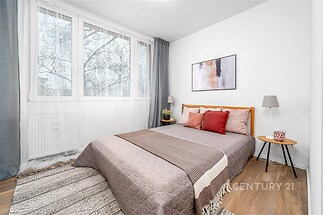 Prostorná ložnice s moderními dřevěnými podlahami, velkými okny a minimalistickým stylem nabízí světlé prostředí k relaxaci.