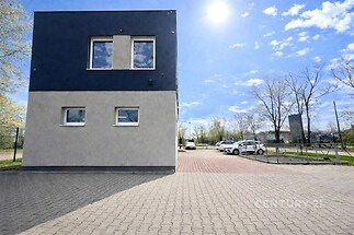 Moderní budova s parkovacími místy, úhledná fasáda, udržovaná dlažba, slunečný den vytváří světlou atmosféru.