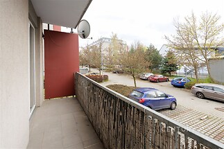 Balkon s dlažbou a bambusovým zábradlím, s výhledem do klidné ulice, vhodný pro relaxaci nebo pěstování rostlin.