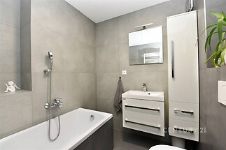 Moderní koupelna s dlažbou, bílými skříňkami a zrcadlem nad umyvadlem, nabízí elegantní a funkční interiér pro pohodlné bydlení.