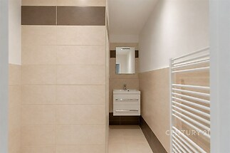 Koupelna s moderními dlažbami, světlým nádechem a praktickým topným žebříkem, nabízí elegantní design a kvalitní vybavení.