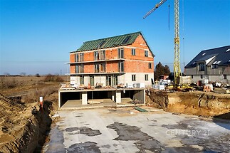 Rozestavěný rodinný dům s červenou cihlovou fasádou, nabízí velká okna a moderní design, nachází se na prostorném pozemku.