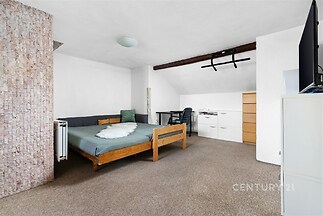 Prostorná ložnice s kobercem a dřevěnou postelí, moderní nábytek, vestavěné skříně, světlý interiér s cihlovým akcentem.