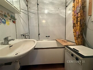 Koupelna s vanou, bílým umyvadlem a dřevěným dekorem, obložení z dlaždic, zavěšené sprchové závěsy, jasné osvětlení, moderní úprava.
