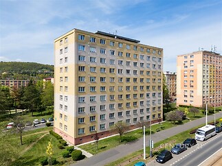 Panelový bytový dům s rekonstruovanou fasádou, obklopený zelení a blízkostí parkování, ideální pro moderní městské bydlení.