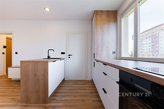 Moderní kuchyň s dřevěnou pracovní deskou, vestavěnými spotřebiči a parketovou podlahou poskytuje světlé a funkční prostředí.
