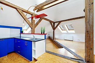 Podkrovní kuchyň s modrými skříňkami, dřevěnými trámy a světlou parketovou podlahou, moderní interiér s velkými střešními okny.