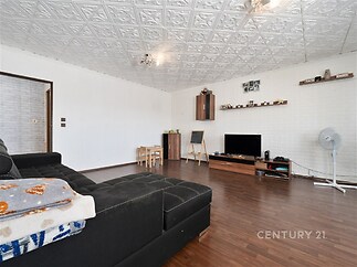 Prostorný obývací pokoj s dřevěnou podlahou, moderním nábytkem a velkou sedačkou, světlý interiér s ozdobným stropem a minimalistickou výzdobou.