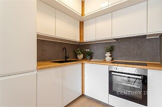 Moderní kuchyň, světlé skříňky s dřevěnou pracovní deskou, elegantní černá armatura, vestavěná trouba, minimalistický design