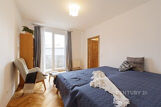 Prostorná ložnice s parketovou podlahou a velkými okny, moderní design a dřevěné dveře poskytují světlé a útulné prostředí.