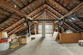 Prostorná půda s dřevěnými trámy a betonovou podlahou, ideální pro úpravu na obytný prostor, nabízí dostatek přirozeného světla a skladovacího prostoru.