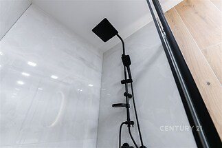 Moderní koupelna s černou sprchovou hlavicí, lesklá dlažba a moderní design, dodávají elegantní vzhled.