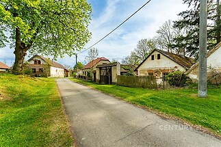 Klidná venkovská ulice lemovaná staršími domy s tradičními štíty a zelení; ideální pro milovníky přírody a historické architektury.