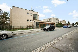 Venkovní pohled na moderní rodinný dům s garáží, čistá fasáda, klidná rezidenční ulice, upravená předzahrádka, dobrý stav.