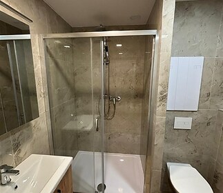 Koupelna s moderními obklady, sprchovým koutem a plovoucí podlahou, obsahuje také nástěnnou toaletu a umyvadlo s úložnou skříňkou.