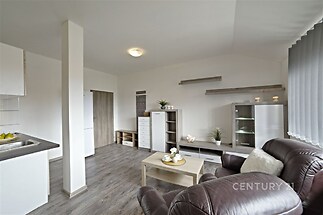 Světlý obývací pokoj s moderními prvky, plovoucí podlahou a velkými okny, nabízí komfortní prostor v rekonstruovaném bytě.