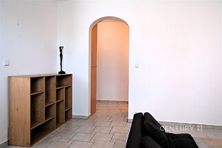 Obývací pokoj s dlažbou a dřevěným regálem, moderní styl, světlý prostor s klenutým průchodem do další místnosti.