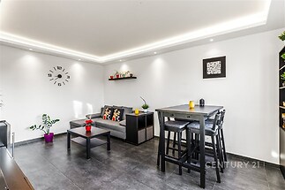 Moderní obývací pokoj, dlážděná podlaha, velká okna, minimalistický design, vestavěné osvětlení, zrekonstruovaný stav, pohodlný nábytek.