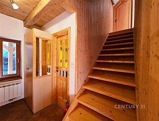 Dřevěné schodiště s dlažbou v přízemí, které vede do patra. Dřevěné obložení stěn dodává rustikální styl, přirozené světlo zajišťují okno.