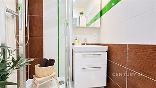 Kompaktní koupelna s moderním designem, dlažbou a sprchovým koutem. Světlé obklady doplněné zelenými akcenty vytvářejí svěží atmosféru.