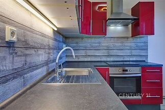 Moderní kuchyň s červenými skříňkami, dřevěným obkladem a vestavěnými spotřebiči, elegantní deska z kamene, ideální pro milovníky stylové kuchyně.