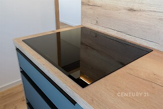 Moderní kuchyň s indukční deskou, dřevěná pracovní deska a vestavěné skříně, minimalistický styl.