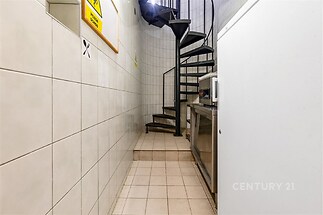 Úzká chodba s točitým schodištěm, dlažba na podlaze a světlé keramické obklady na stěnách vytvářejí funkční prostor.