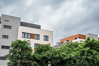 Moderní bytový dům s velkými okny, elegantní fasáda ze světlého materiálu, okolní zeleň dodává příjemný vzhled
