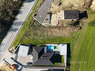 Pohled na moderní rodinný dům s dřevěnou terasou, zahradou a přilehlou garáží, obklopený přírodou.