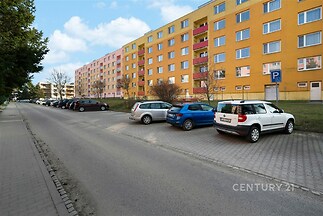Vícepodlažní bytový dům s barevnou fasádou, okolí s parkovacími místy a zelení, vhodné pro rodiny, klidná lokalita, dobrá dostupnost.