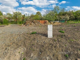 Stavební pozemek s rovinným terénem, obklopený zelení a ovocnými stromy, ideální pro výstavbu rodinného domu nebo rekreačního objektu.