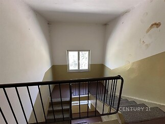 Schodiště s kobercovým povrchem, kovovým zábradlím a velkým oknem, které poskytuje přirozené světlo, ideální pro rekonstruované prostory.