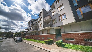 Moderní bytový dům s balkony, světlá fasáda, okolní udržovaná zeleň, klidná rezidenční oblast, velká okna, kvalitní materiály, nový stav