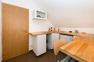 Kompaktní kuchyň s dřevěnou pracovní deskou, moderním stylem a dlažbou v přízemním bytě.