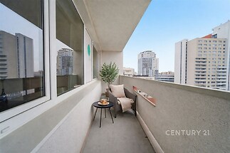 Úzký balkon s výhledem na město, betonová podlaha, velká okna, moderní design, ideální pro relaxaci a posezení.