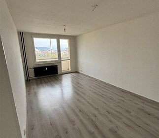 Obývací pokoj s parketovou podlahou, velká okna a světlý prostor, moderní styl a dostatek přirozeného světla.
