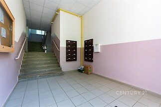 Vstupní hala bytového domu s dlažbou, poštovními schránkami a schodištěm, které vede do vyšších pater, čisté a světlé prostředí.