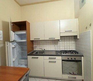 Malá kuchyň s dlažbou, vestavěnými spotřebiči a bílými skříňkami, v dobrém stavu, poskytuje funkční a útulný prostor pro vaření.