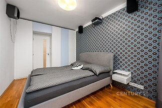 Prostorná ložnice s parketovou podlahou, vestavěnými skříněmi a moderními tapetami na stěně, nabízí elegantní a útulný prostor k odpočinku.