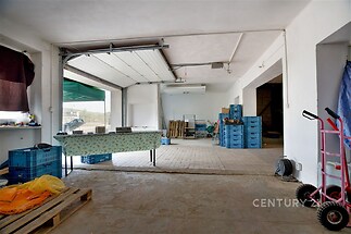 Průmyslový prostor s betonovou podlahou, velkými vraty a uskladněním. Vhodný pro podnikání či skladování, světlý a prostorný.