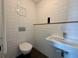 Moderní koupelna s bílými dlaždicemi, závěsným WC a umyvadlem. Elegantní design, čisté linie, ideální pro současný bytový interiér.