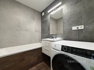Moderní koupelna s dlažbou, vestavěnou vanou a praktickou pračkou. Elegantní design a kvalitní materiály dodávají místnosti stylový vzhled.