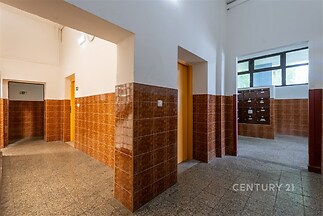 Vstupní hala s dlažbou a velkými okny, vybavená poštovními schránkami, nabízí prostorný a světlý prostor v bytovém domě.
