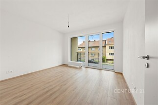 Světlý obývací pokoj s parketovou podlahou, velkými okny a moderním designem, poskytuje prostorné a elegantní bydlení.
