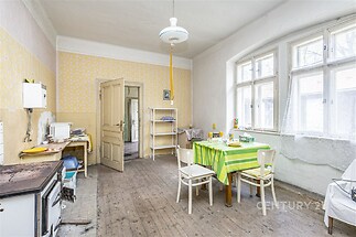 Prostorná kuchyň s dřevěnou podlahou, velkými okny a světlým nábytkem, nabízí možnost rekonstrukce a moderní úpravy.
