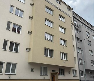 Exteriér rekonstruovaného bytového domu s novou fasádou a plastovými okny, nacházející se v městském prostředí s parkováním.