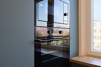 Moderní kuchyň s vestavěnou troubou a velkými okny, která poskytují dostatek světla, elegantní dřevěná pracovní deska