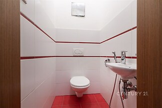 Malá světlá toaleta s červenou dlažbou, moderní bílou sanitou a obkladem. Jednoduchý a čistý design, ideální pro menší prostory.