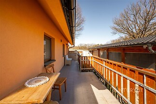 Prostorná terasa s dlažbou, dřevěným zábradlím a výhledem na zahradu, vhodná pro venkovní posezení a relaxaci, v klidném prostředí.